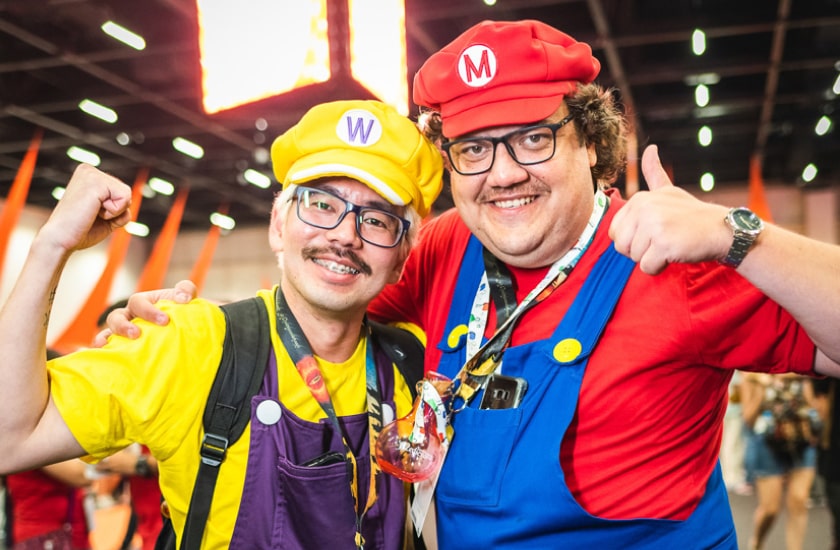 Na imagem, dois amigos vestidos de Mario Bros como cosplay na CCXP. Um de vermelho, azul, óculos e boina. Prepare-se para cosplays incríveis na CCXP22!